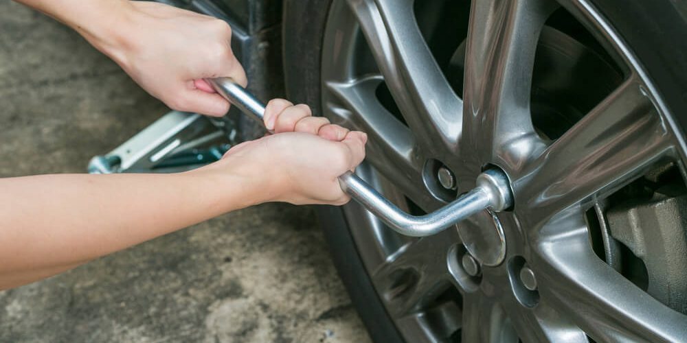 close up of hands loosening lug nuts with a wrench.